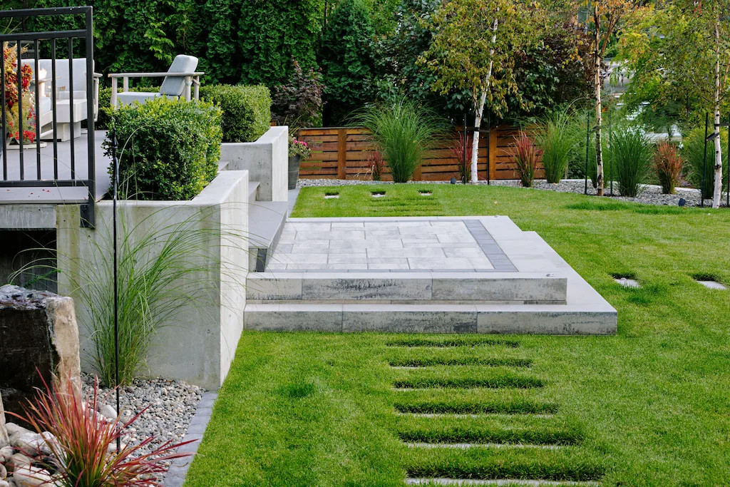 Modern home steps with a retaining wall surrounded by greenery a green lawn, and paver pathway