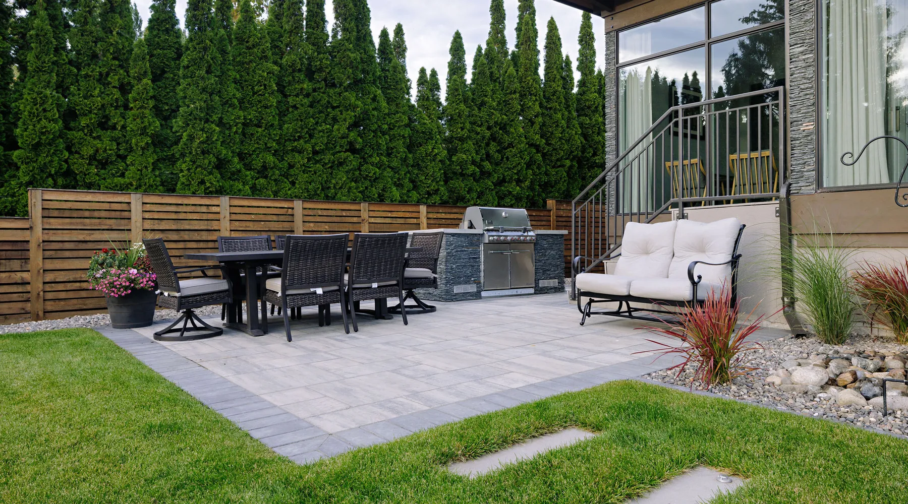 paver stones walkway green grass shrubs and grasses next to a bbq